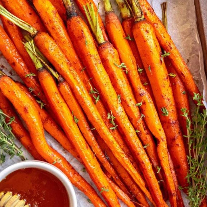 Honey glazed carrots served on a wooden tray with small bowls of honey and fresh thyme on either side.