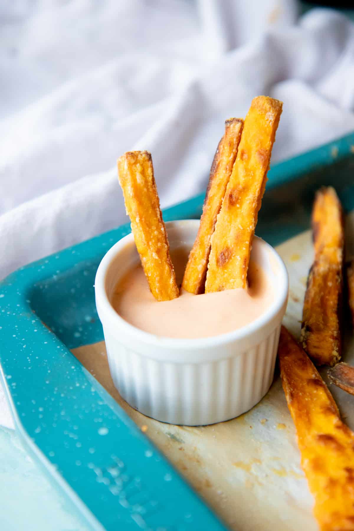 Three crispy sweet potato fries sticking out of a ramekin of dipping sauce. 