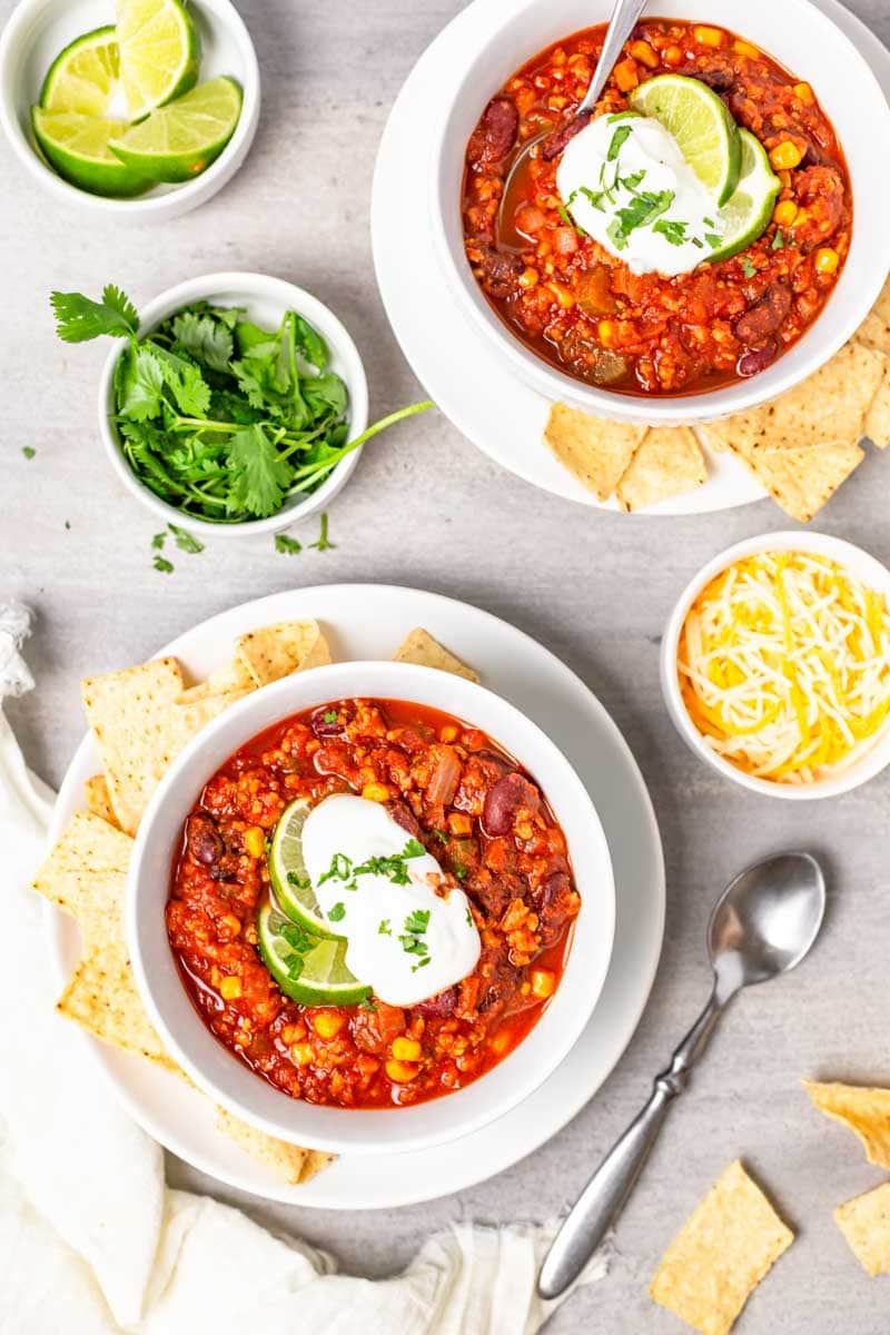 Overhead of two bowls filled with chili surrounded by fresh garnishes and tortilla chips.