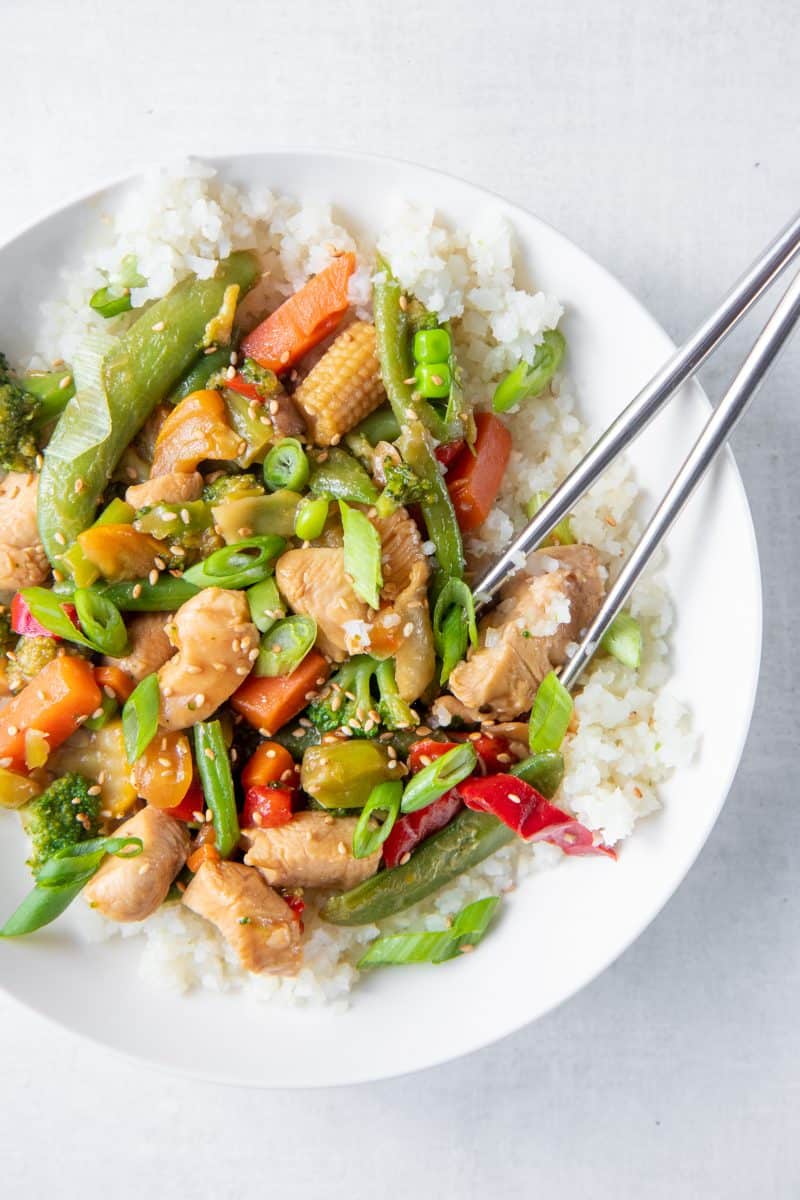 Chopsticks grab a bite out of a bowl of healthy chicken stir fry.