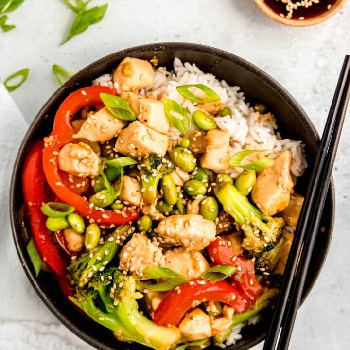 A teriyaki chicken rice bowl served with chopsticks and a small bowl of extra sauce alongside.