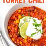 Close-up of full bowl of taco chili on a plate with spoon and tortilla chips. A text overlay reads, "The Best Ever Turkey Chili."