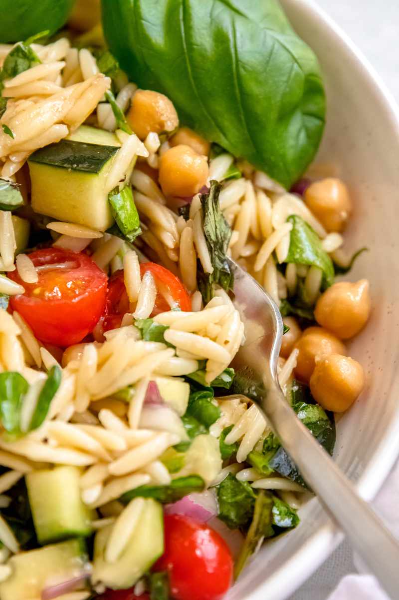 Tight view of a fork digging into a bowl of pasta salad loaded with summer vegetables.