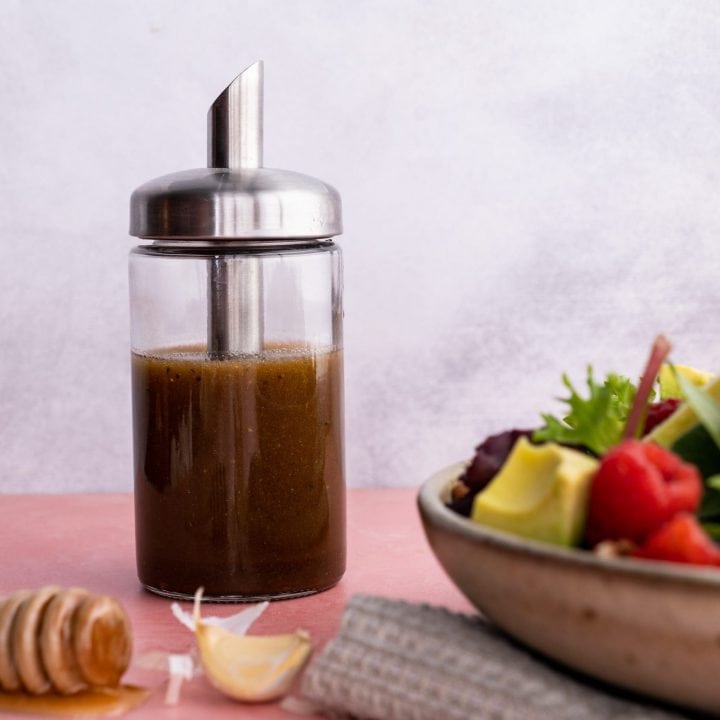 A glass cruet filled with balsamic vinaigrette stands beside a salad bowl filled with fresh ingredients.