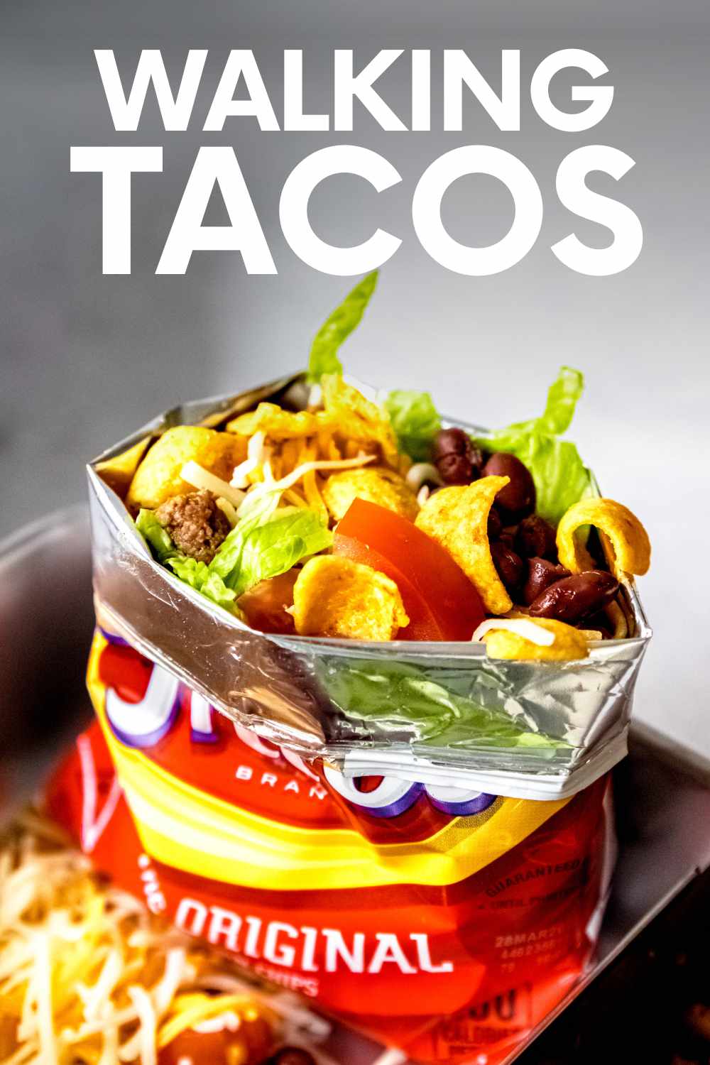 An assembled walking taco rests in a stainless steel lunch box. A text overlay reads, "Walking Tacos."