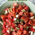 A large serving bowl of watermelon basil salad on a light counter with a blue and white striped kitchen linen. A text overlay reads, "Watermelon Basil Salad."