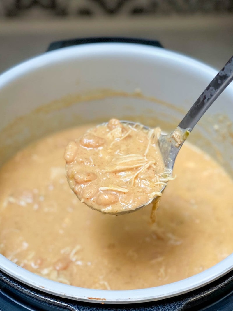 A metal ladle scoops white chicken chili from an Instant Pot.