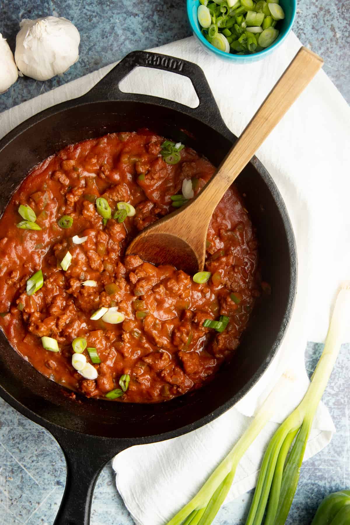 A wooden spoon sits in a beef sauce in a cast iron skillet.