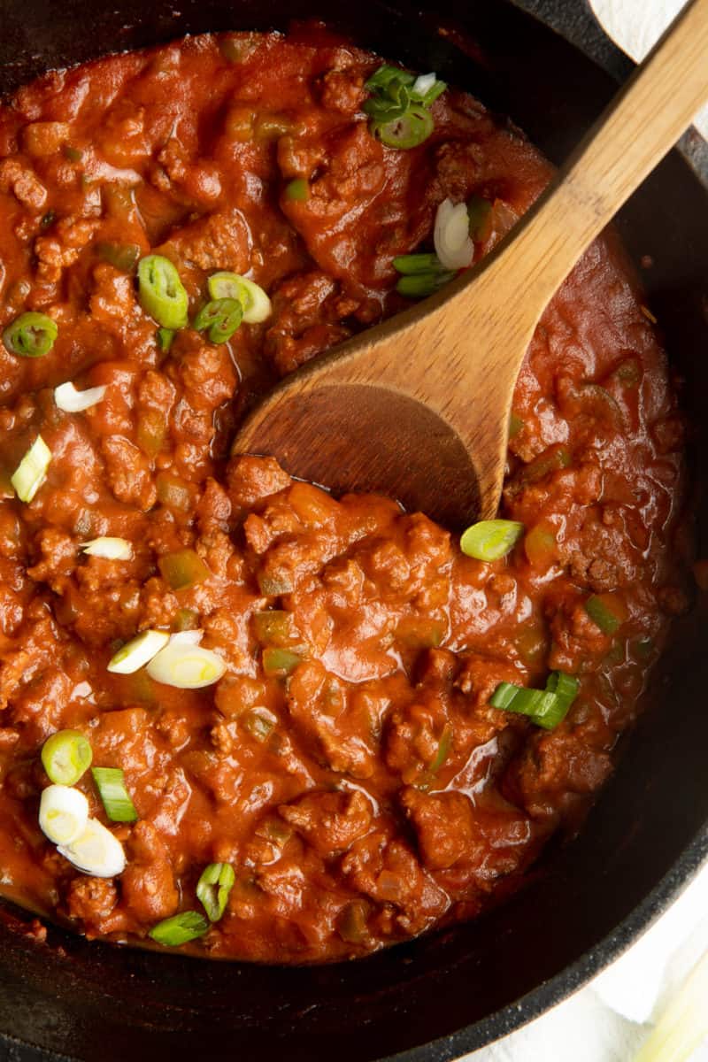 A wooden spoon stirs filling for Sloppy Joes in a cast iron skillet.