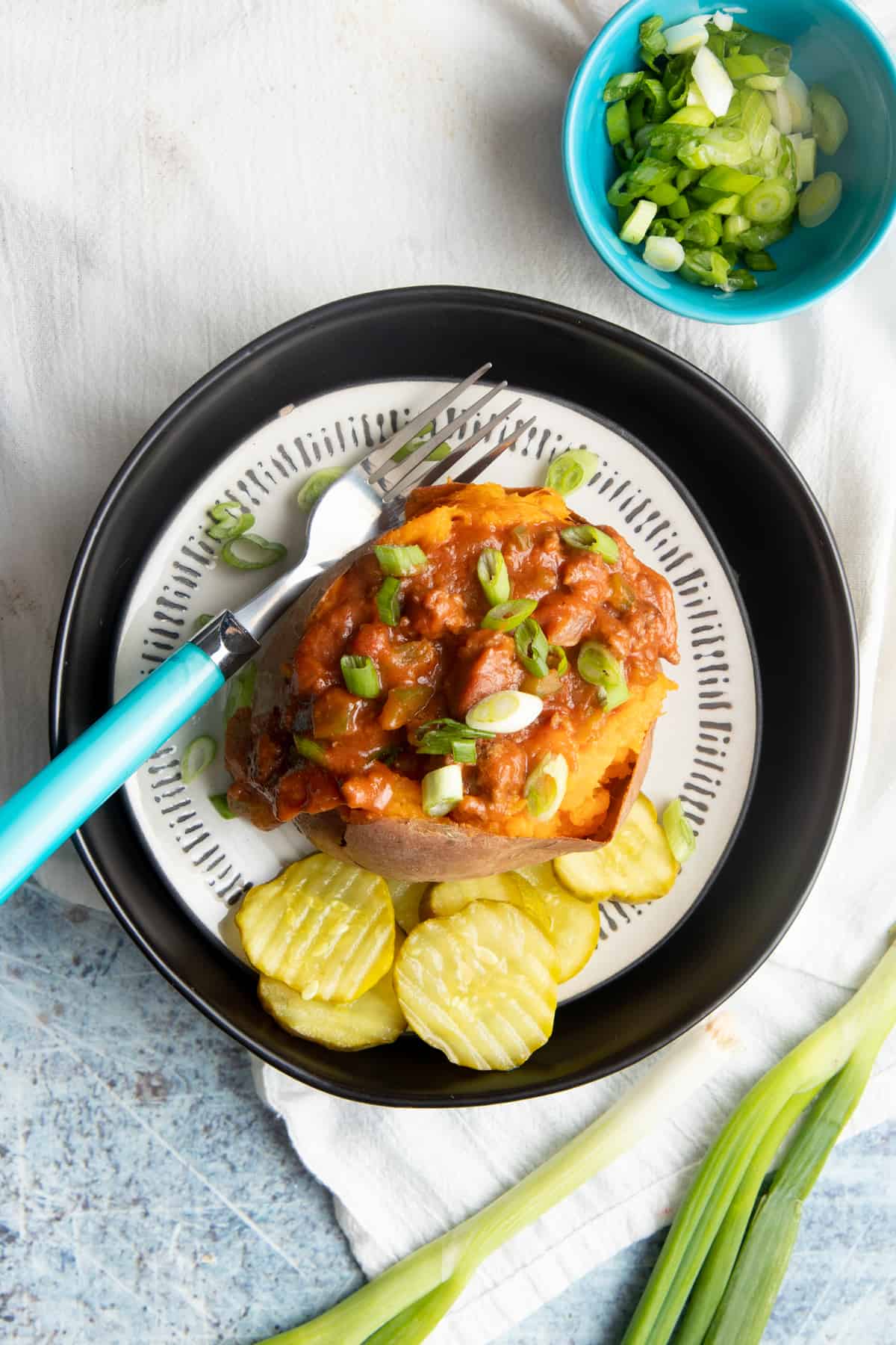 Sweet potato stuffed with a beef sauce on a plate, with sliced pickles on the side.